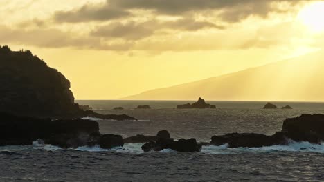Golden-hour-glow-spreads-across-misty-sky-with-ocean-waves-crashing-on-rocks-in-Hawaii