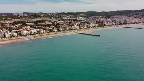 Sitges,-Spanien,-Zeigt-Die-Küste-Und-Das-Stadtbild-Mit-Bergen-Im-Hintergrund,-Luftaufnahme