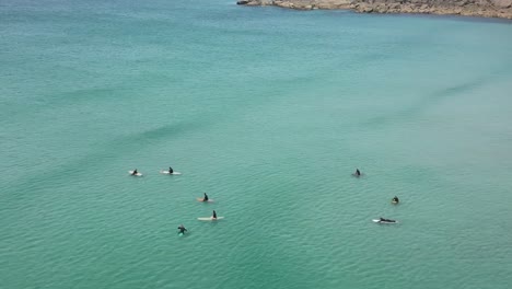 Surfers-Paddling-and-Waiting-Over-Ocean-Waves-with-Turquoise-Waters-in-Cornwall,-UK