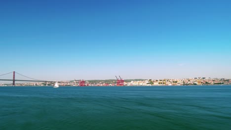 Timelapse-video-of-the-iconic-25-de-Abril-Bridge-with-the-Lisbon-cityscape-from-a-distance-through-the-Tagus-River-on-a-sunny-day-in-Portugal