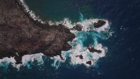 Luftaufnahme-Von-Oben-Nach-Unten-Von-Weißen-Wellen-Aus-Tiefblauem-Ozeanwasser,-Die-Auf-Erodierte-Klippen-Krachen