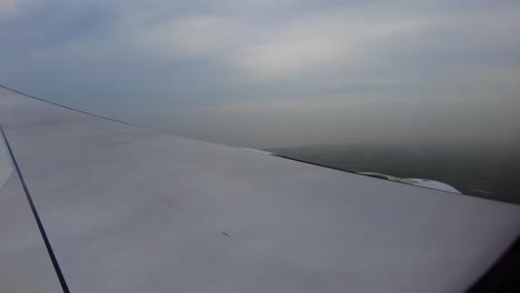 Luftaufnahme-Aus-Dem-Flugzeugfenster-Zeigt-Flügel-Und-Wolken-Mit-Landschaft-Darunter-Während-Des-Sinkflugs