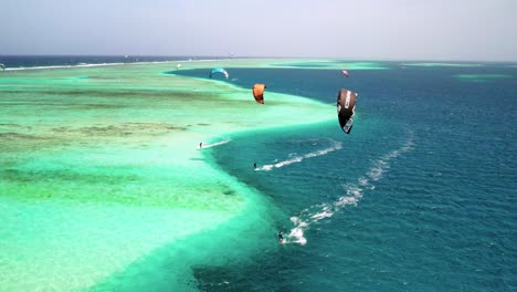Kite-surfers-gliding-over-the-clear-blue-waters-by-a-coral-reef-in-los-roques,-aerial-view