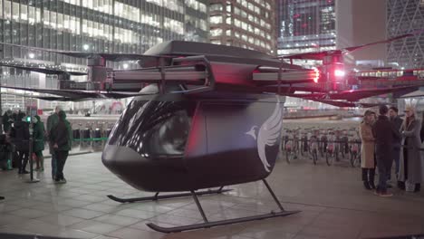 Futuristic-real-drone-taxi-in-Canary-Wharf-Square-London-with-its-lights-on-with-curious-people-around-it