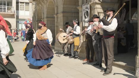 Regionale-Tänzer-In-Traditioneller-Tracht-Und-Maske-Tanzen-Mit-Männern,-Die-Instrumente-Spielen,-Unter-Der-Sonne-In-Lugo,-Galicien,-Spanien