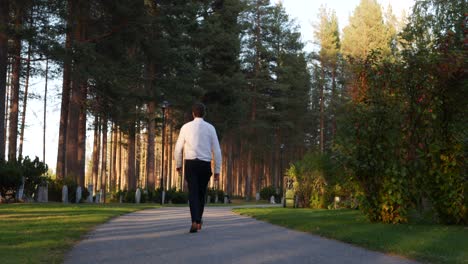 Mann-Zu-Fuß-In-Richtung-Grabsteine-In-Einem-Gartenfriedhof-In-Schweden-An-Einem-Sonnigen-Nachmittag