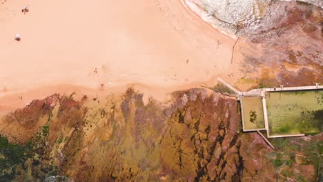 Cinematic-top-down-drone-aerial-view-slowly-moving-across-a-rock-pool-alongside-the-beach-in-Sydney,-Australia