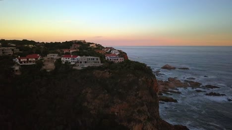 Flying-over-Villas-sitting-on-Knysna-Heads-Cliff-Edge,-Golden-Hour,-South-Africa,-Aerial-Forward-Motion