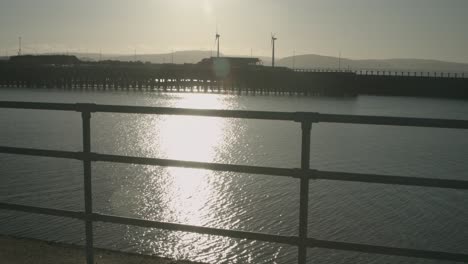 Windturbinen-Im-Frühen-Morgenlicht-Des-Sonnenaufgangs-Mit-Wunderschöner-Sonnenreflexion-Auf-Dem-Wasser