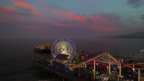 Beautiful-aerial-fly-over-ferris-wheel-in-Santa-Monica-during-sunrise-with-smiley-face-lights