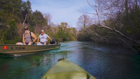 Zwei-ältere-Amerikanische-Männer-In-Einem-Boot-Fahren-Mit-Einem-Kajak-Im-Magischen,-Klaren-Blauen-Und-Türkisfarbenen-Wasser-Des-Weeki-Wachee-Springs-State-Park-River-In-Florida-Vorbei,-Der-Heimat-Von-Seekühen-Und-Wildtieren