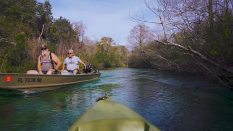 Dos-Ancianos-Estadounidenses-En-Un-Bote-Pasan-Por-Un-Kayak-En-Las-Mágicas-Aguas-Azules-Y-Turquesas-Del-Río-Weeki-Wachee-Springs-State-Park-En-Florida,-Hogar-De-Manatíes-Y-Vida-Silvestre.