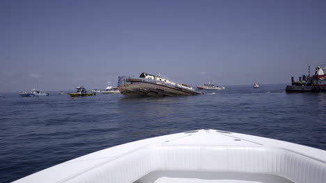 Large-boat-sinking-fast-in-ocean-with-boats-spectating,-wide-shot