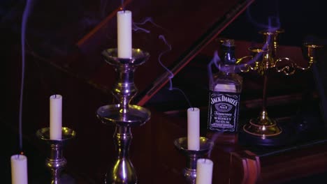 Langsam-Rotierende-Ansicht-Eines-Dunklen-Raums-Mit-Rauchenden-Kerzen-In-Kandelabern-Und-Einer-Whiskyflasche-Auf-Einem-Klavier