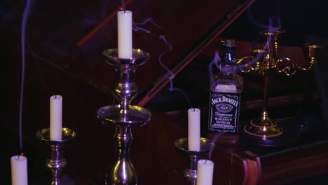 Vista-Giratoria-Lenta-De-Una-Habitación-Oscura-Con-Velas-Humeantes-En-Candelabros-Y-Una-Botella-De-Whisky-Sentada-En-Un-Piano