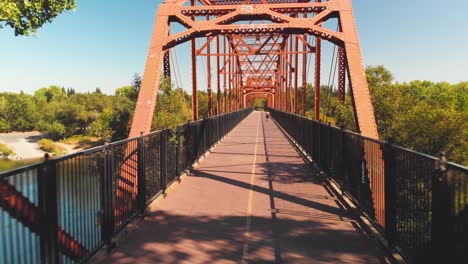 Mann,-Der-Mit-Einem-Hund-Auf-Der-Fair-Oaks-Bridge-über-Den-American-River-In-Kalifornien-Spazieren-Geht---Luftaufnahme-Einer-Drohne,-Die-Durch-Die-Brücke-Fliegt