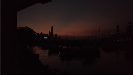 Weitwinkelaufnahme-Des-Sonnenuntergangs-Im-Zeitraffer,-Verankerte-Boote-Auf-Dem-Wasser,-Skyline-Von-Hongkong