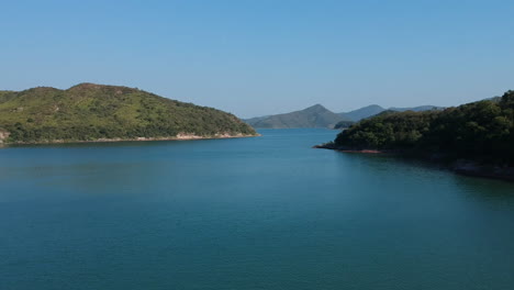 Drone-Flyover-of-Reservoir-in-Hong-Kong,-Island-Coastline-in-Background