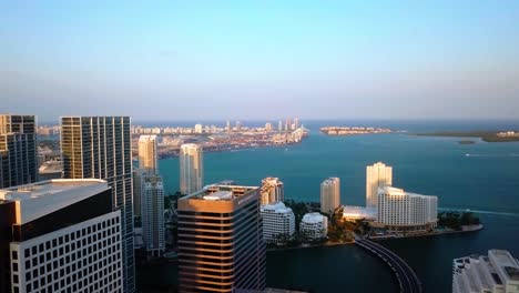 Aerial-view-over-high-rise-buildings,-towards-the-Brickell-key-and-the-sea,-during-sunrise,-in-Miami,-Florida,-USA---rising,-drone-shot