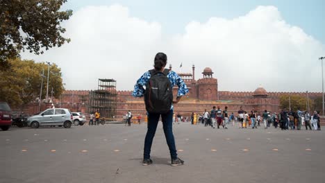 Chica-Con-Mochila-De-Pie-Contra-El-Antiguo-Monumento-Histórico-Fuerte-Rojo-Famoso-Destino-Turístico-En-Nueva-Delhi,-India,-Asia,-Plano-General