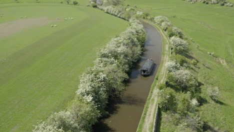 An-aerial-view-of-a-canal-boat-traveling-down-a-canal-surrounded-by-Yorkshire-countryside-on-a-sunny-spring-day