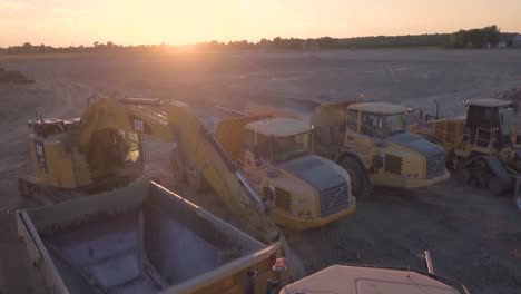 Drone-flying-over-parked-heavy-machinery-against-the-setting-sun-in-the-background