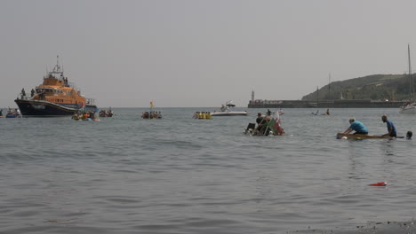 Local-business-teams-turning-halfway-at-the-Newlyn-raft-race-charity-fun-outdoors-event,-Cornwall