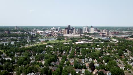 Wide-aerial-shot-slowly-moving-forward-and-down-with-the-city-of-Saint-Paul,-Minnesota-on-the-horizon-by-the-Mississippi-river-surrounded-by-trees-and-houses-on-a-sunny-day