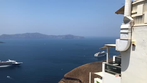 Wide-Shot-Of-The-Islands-in-Santorini-Greece-from-The-City-of-Thira-Next-to-a-White-Building-With-Two-Ferries,-Lots-of-Birds-and-a-Butterfly-Flying-By