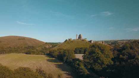 Drone-Flying-over-Castle-Ruins-on-a-green-Mountain-at-sunset,-England-UK