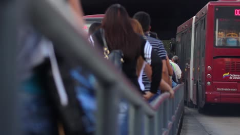 Queue-of-passengers-at-bus-station-filmed-from-behind-at-hip-height-along-metal-barrier