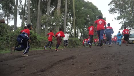 Eine-Gruppe-Afrikanischer-Kinder-In-Roten-Hemden-Spielt-Ein-Sportrennen-Und-Rennt-In-Zeitlupe-Zum-Ziel-Eines-Marathons-Auf-Einer-Schlammigen-Straße-Im-Dschungelwald-Von-Tansania