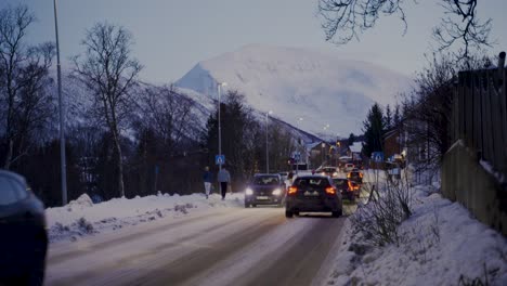 Statische-Aufnahme-Von-Autos,-Die-Auf-Einer-Verschneiten-Straße-Mit-Riesigen-Schneebedeckten-Bergen-Im-Hintergrund-Fahren