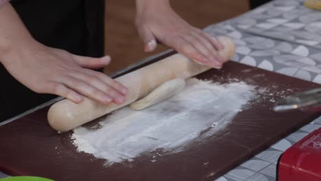 Female-rolling-out-dough-with-a-wooden-rolling-pin-on-a-bed-of-flour,-preparing-food