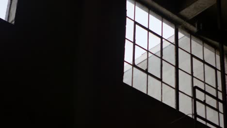 A-pan-shot-of-a-large,-bright-window-from-within-a-dark-industrial-building