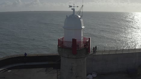 Aerial-orbits-lighthouse-at-wharf-breakwater-on-calm,-sunny-day