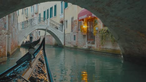Traditional-italian-gondola-passing-under-bridges-on-narrow-venetian-canal
