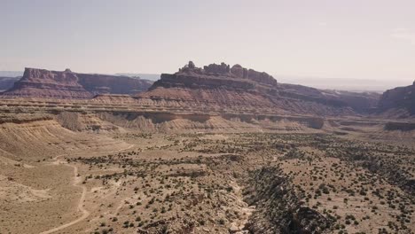 Incredible-beautiful-drone-footage-flying-away-from-mesa-rock-over-desert-valley,-bushes-and-landscape-in-Black-Dragon-Canyon-in-Green-River,-Utah,-United-States