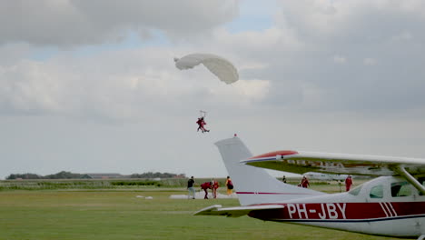 A-tandem-jump-Skydivers-with-open-Parachutes-slowely-glide-down-to-earth-and-lands-behind-a-plane