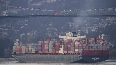 Ein-Frachtschiff-Voll-Beladen-Mit-Containertransportern-Fährt-In-Brockton-Point,-Stanley-Park-In-Vancouver,-British-Columbia,-Mit-Fahrzeugen,-Die-Im-Hintergrund-über-Die-Lions-Gate-Bridge-Fahren---Mittlere-Aufnahme