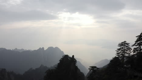 Mountain-valley-reveal-through-trees,-aerial-view-of-sun-rays-over-mountainside-landscape