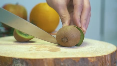 Mano-De-Chica-En-Cámara-Lenta-Cortando-Kiwi-Con-Un-Cuchillo-Afilado-Cortando-Kiwi-Fresco-De-Cerca-En-Una-Tabla-De-Cortar-De-Madera