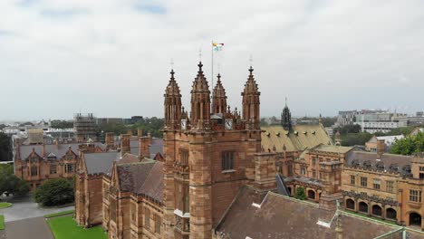 Panoramic-view-of-the-campus-of-the-University-of-Sydney,-Australia,-showing-the-beautiful-architectural-details-of-its-main-building-and-a-flag-blowing-in-the-wind-at-the-highest-point-of-the-roof