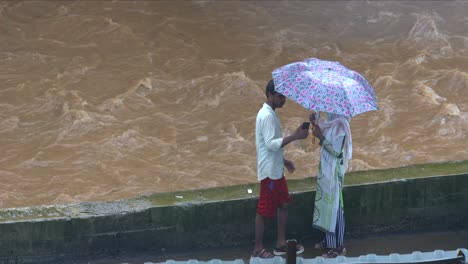Paare-Unter-Einem-Regenschirm-Machen-Selfie-Bei-Starkem-Regen,-Großer-Fluss-Im-Hintergrund,-Mumbai