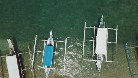 Flying-above-banca-boats-on-a-shore,-the-bird-eye-view-provides-a-great-reveal-of-the-banca's-floating-on-the-edge-of-the-water