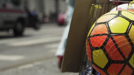 Un-Colorido-Balón-De-Fútbol-En-Primer-Plano-Y-El-Tráfico-Que-Circula-Al-Fondo-En-Feira-De-Santana,-Bahía,-Brasil