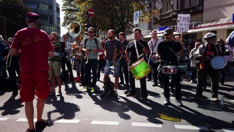 A-brass-band-with-trumpets,-a-tuba-and-drummers-plays-on-the-street-as-a-protest-march-for-action-against-climate-change-and-global-warming-marches-past