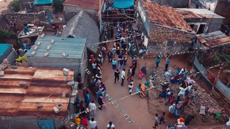 Aldea-Rural-Africana-Celebrando-Una-Fiesta-De-Baile-Nupcial-En-Las-Calles-Con-Banderas-Ondeando-Al-Viento,-Filmada-Desde-Arriba-En-Las-Comoras,-áfrica