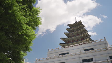 Low-angle-view-of-a-Gyeongbokgung-Palace-structure-in-Seoul-Korea-beyond-a-tree-on-a-clear-day,-wide-shot-dolly-in-slow-motion