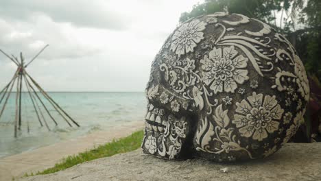 Mexican-sculpted-skull-with-wooden-tipi-structure-on-lagoon-in-background